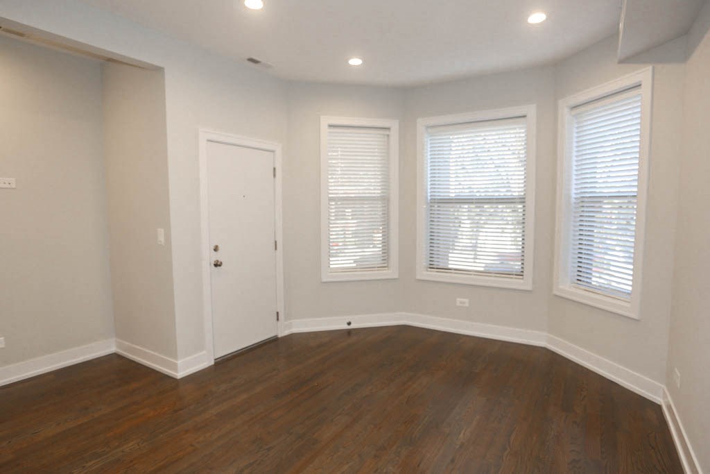 the living room of a house with a wooden floor and three windows