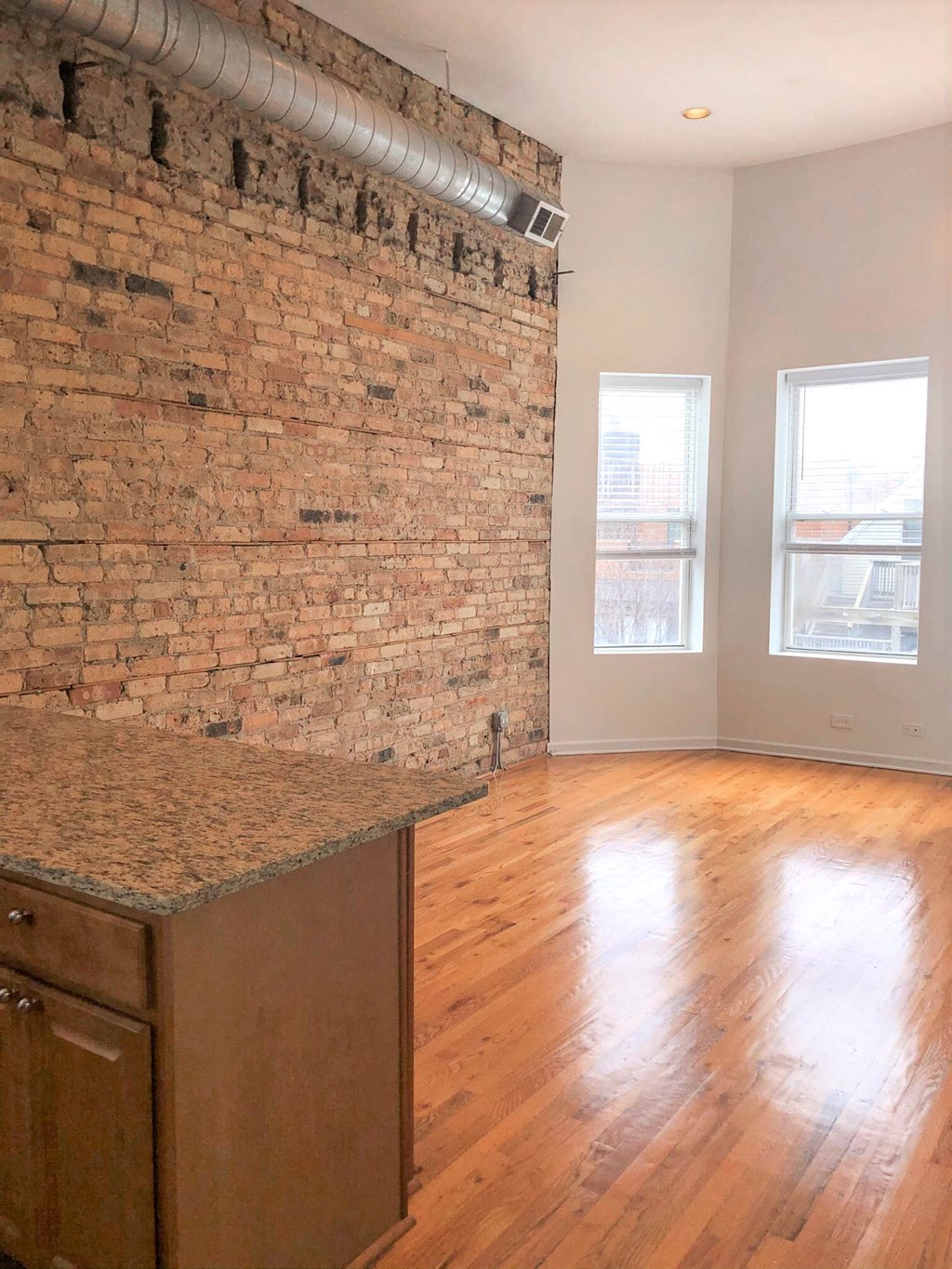 an empty living room with an exposed brick wall and wood floors