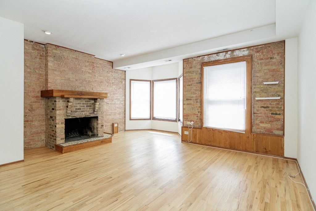 an empty living room with a brick fireplace and wooden floors