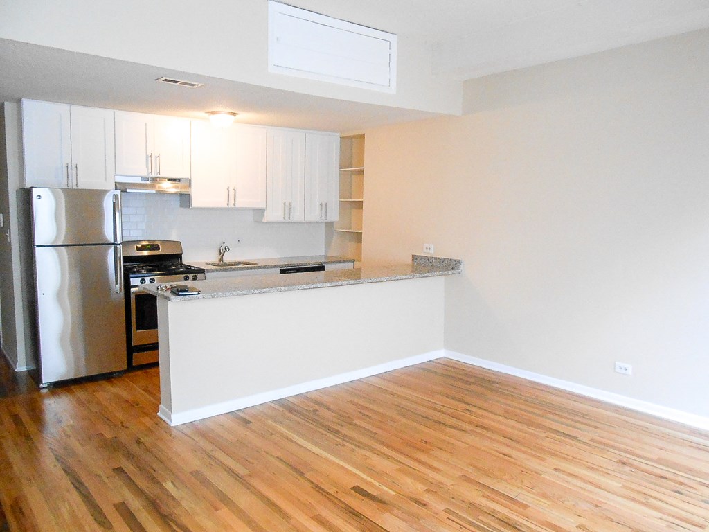 an empty kitchen with a wooden floor and a stainless steel refrigerator