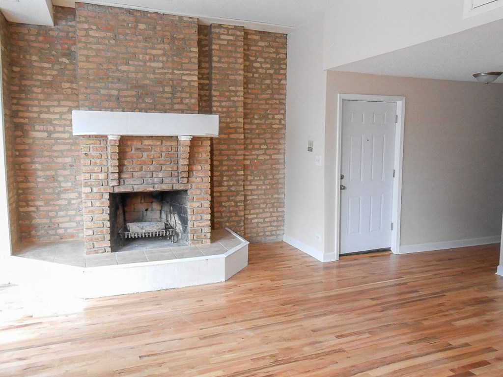 an empty living room with a brick fireplace and wooden floors