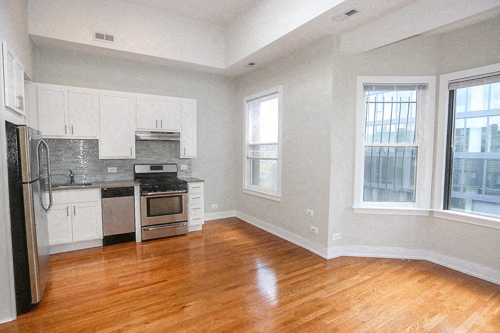 an empty kitchen with a wood floor and white cabinets