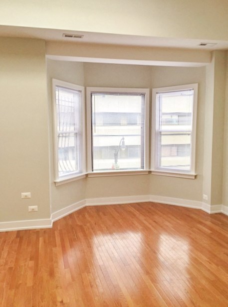 an empty living room with a wooden floor and three windows
