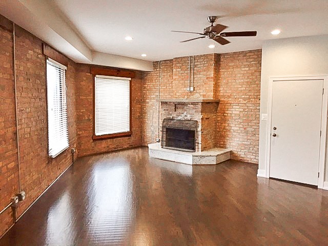 an empty living room with a brick fireplace and wooden floors