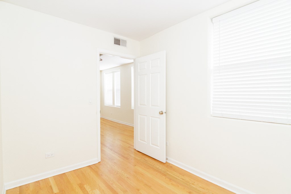 a bedroom with white walls and wood floors and a white door