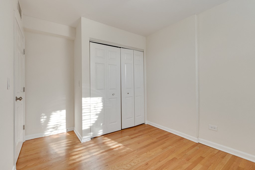 a bedroom with white walls and wood floors and a closet