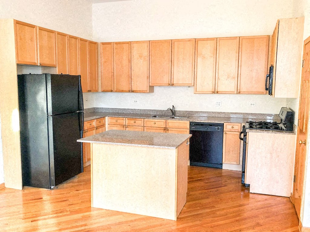 an empty kitchen with wooden cabinets and a black refrigerator