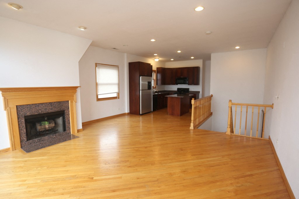 an empty living room with a fireplace and a kitchen