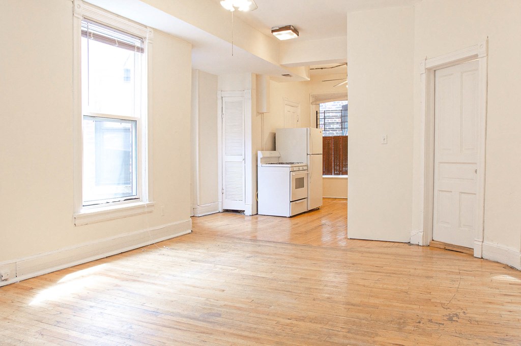 an empty living room with a refrigerator and a window