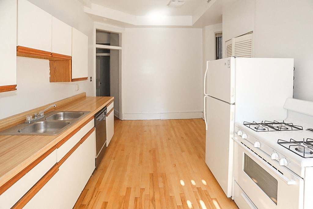an empty kitchen with white appliances and wood flooring