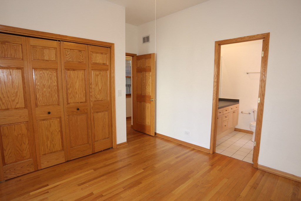 a bedroom and a bathroom with wooden floors and a door to a closet