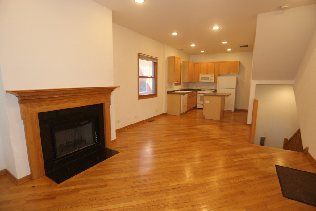an empty living room with a fireplace and a kitchen