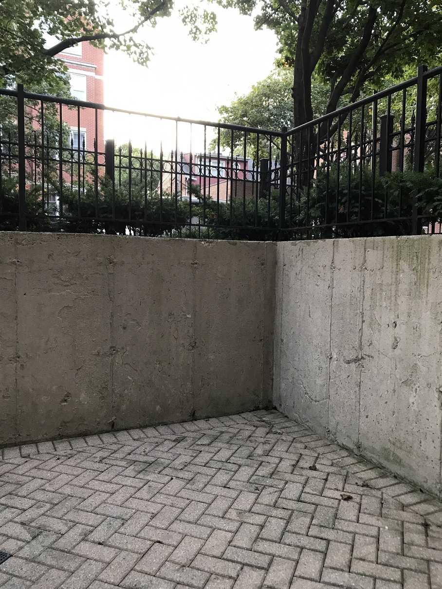 a concrete wall with a black fence and a brick sidewalk