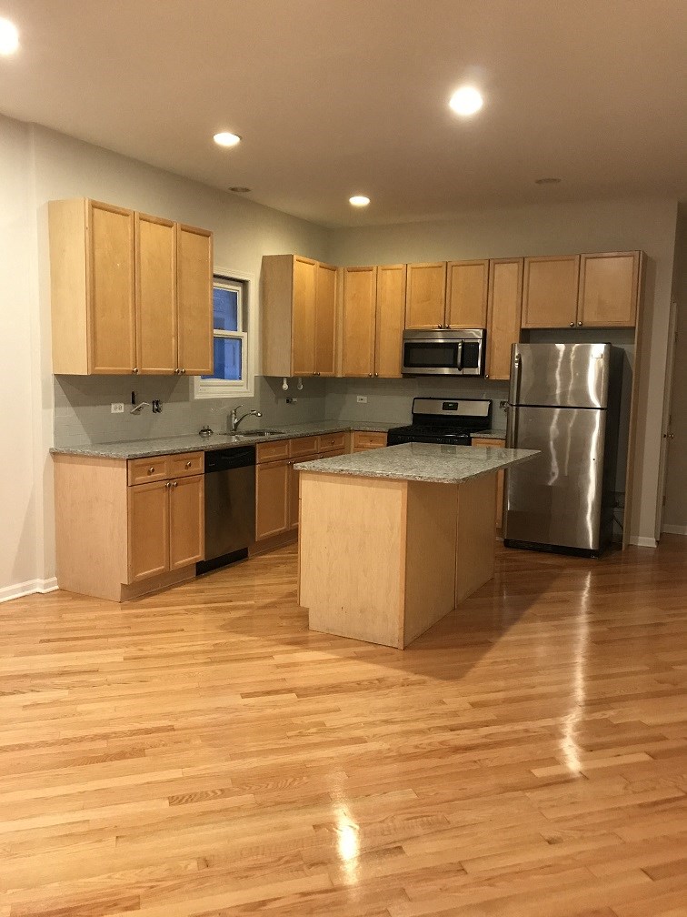 an empty kitchen with wooden floors and stainless steel appliances