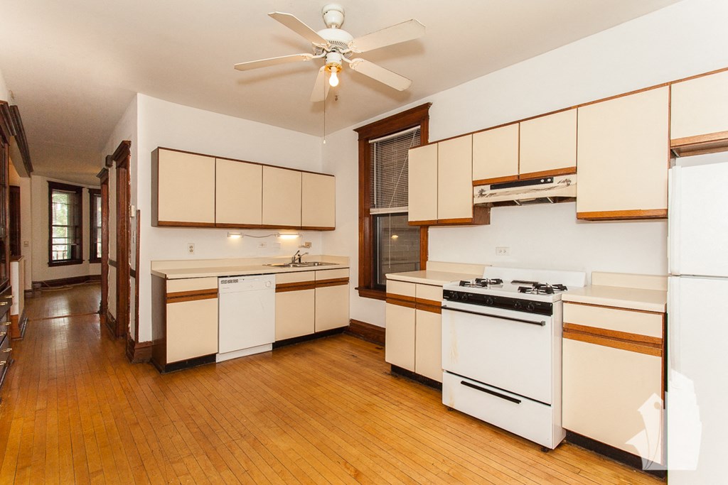 a kitchen with white appliances and wooden floors and a ceiling fan