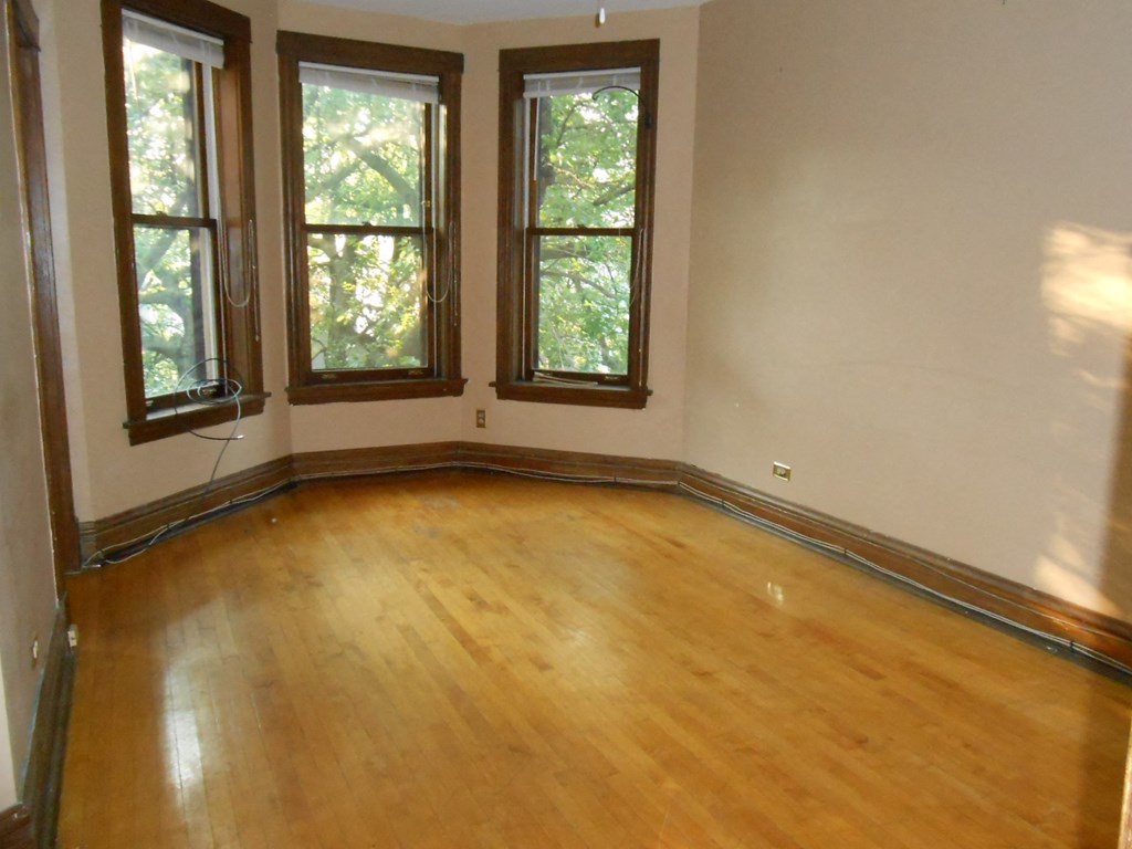 an empty living room with wooden floors and three windows
