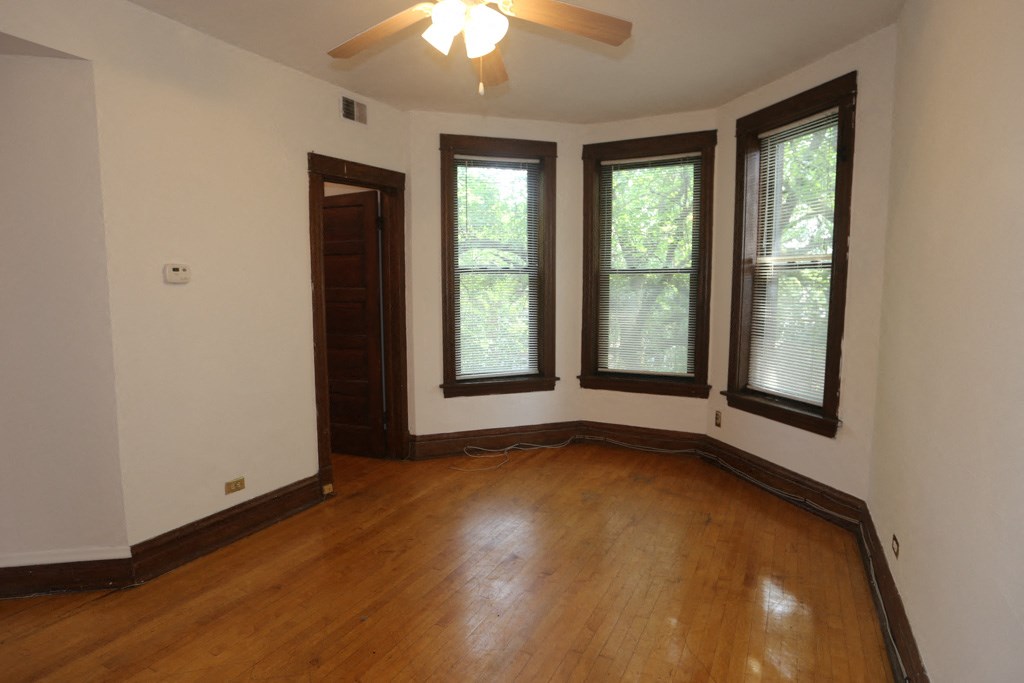 an empty living room with wooden floors and three windows