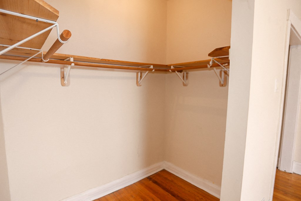 a walk in closet with a wood floor and a white wall with an empty closet