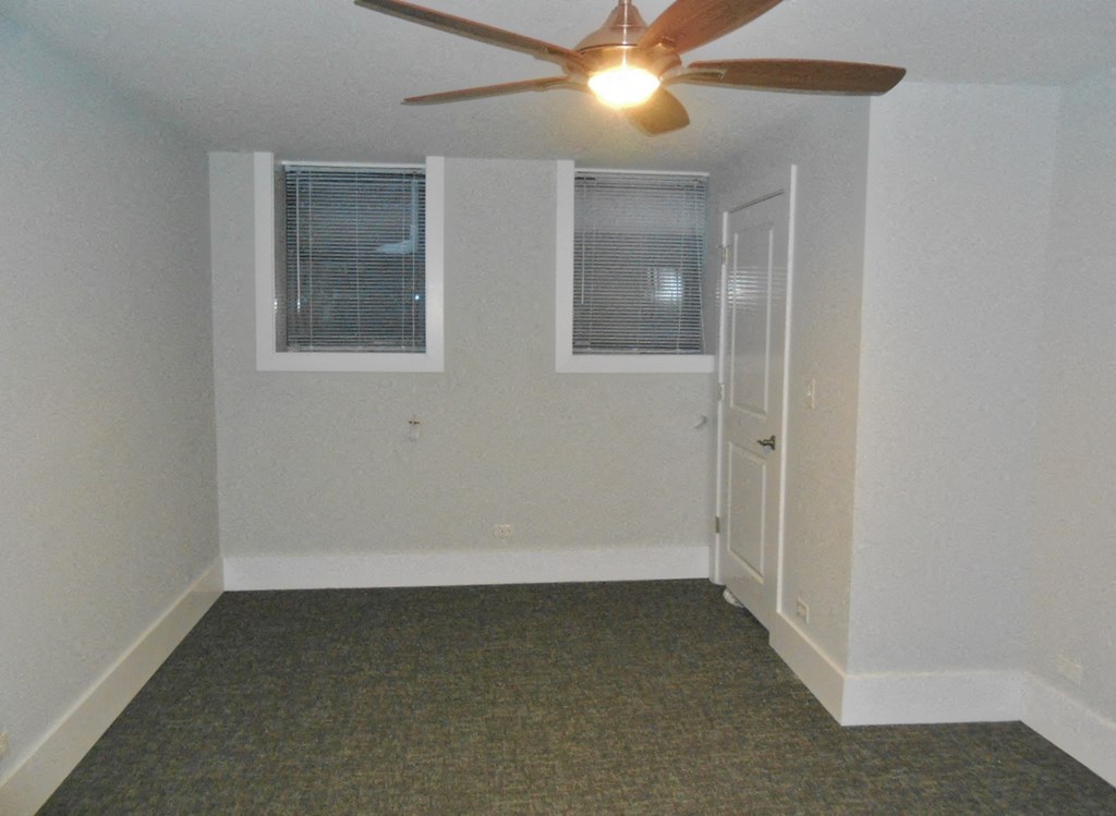an empty room with a ceiling fan and two windows