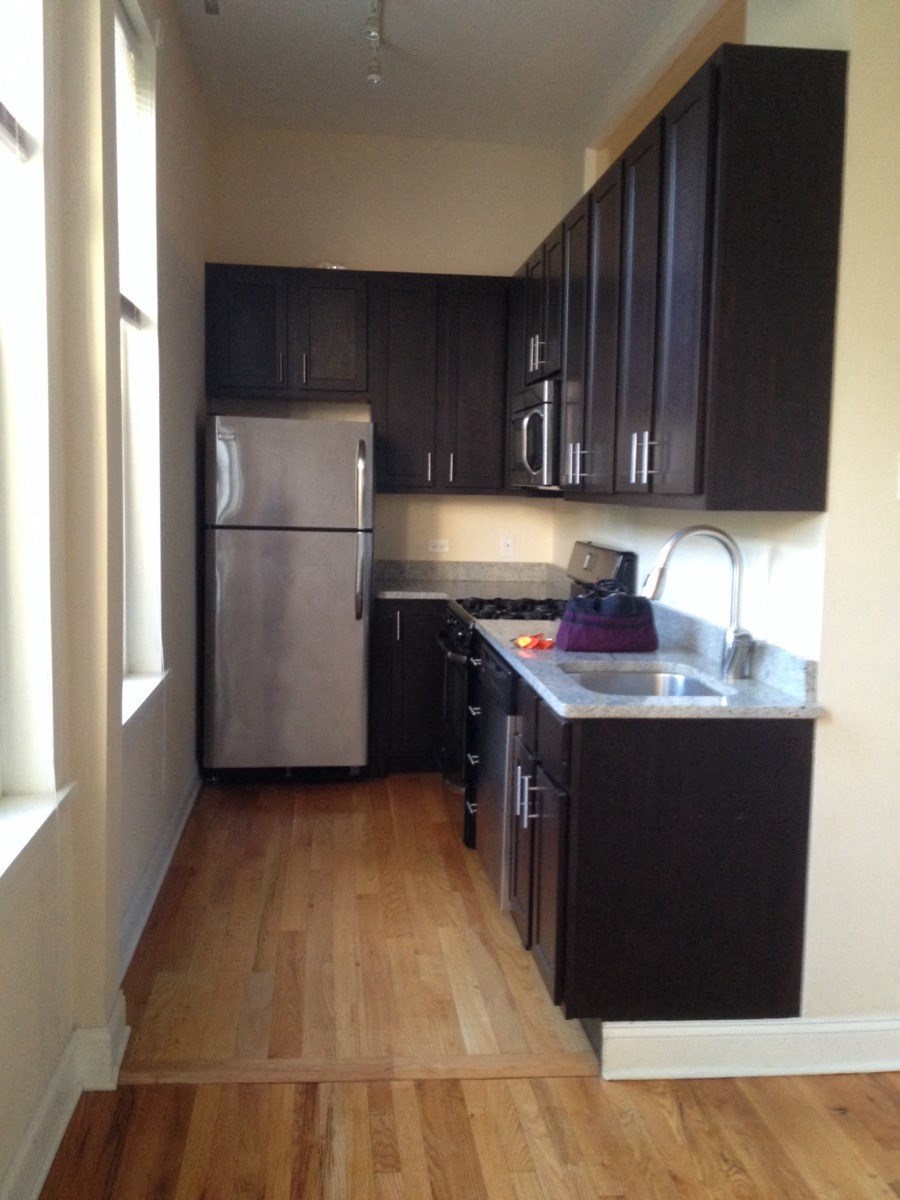 an empty kitchen with black cabinets and a stainless steel refrigerator