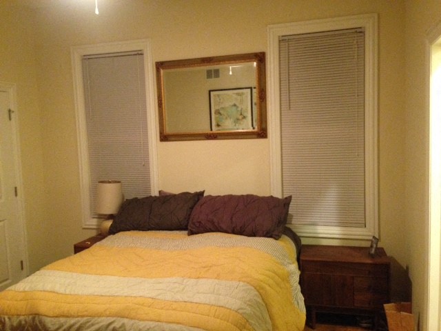 a bedroom with a bed and a mirror and two windows