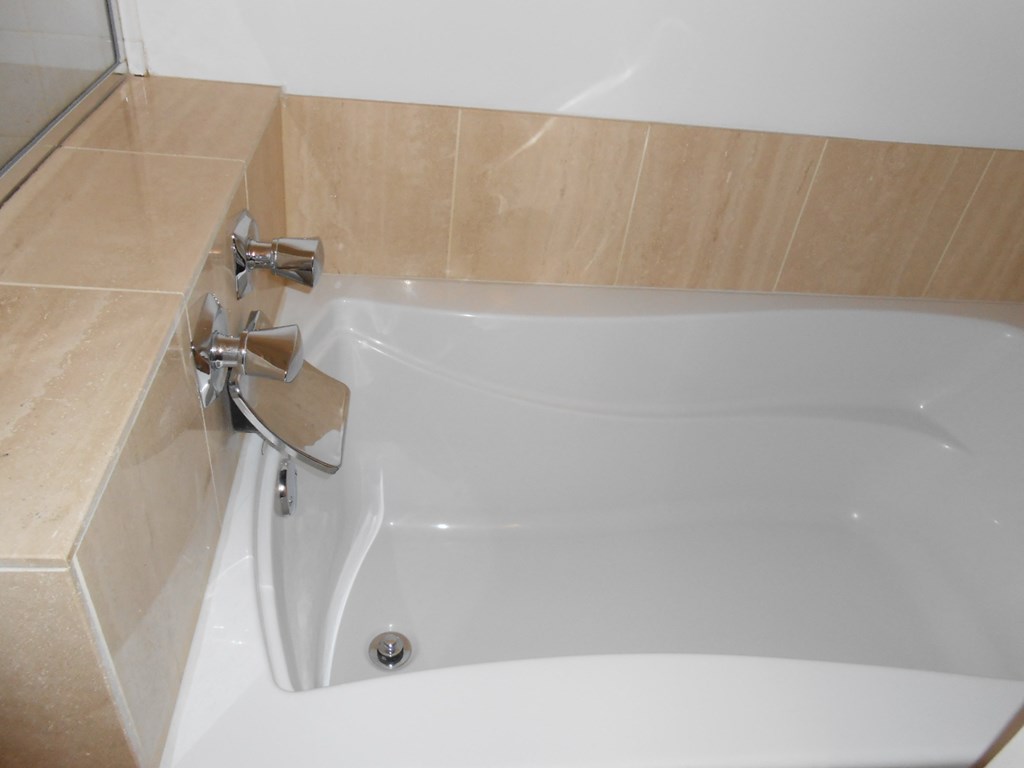 a white bath tub in a bathroom with beige tiles