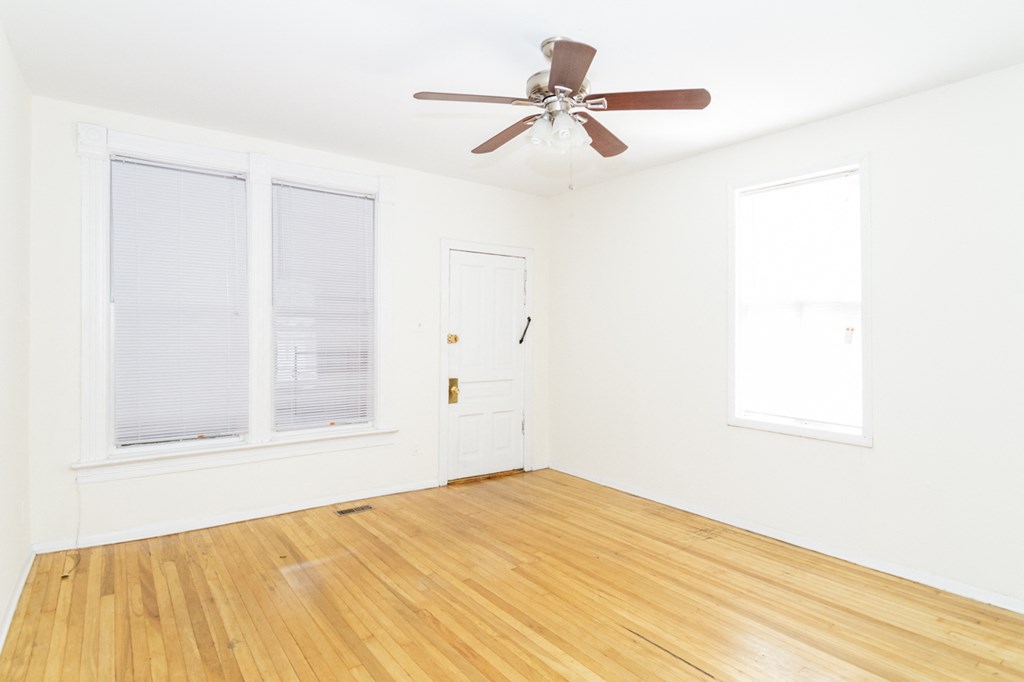 an empty room with a ceiling fan and two windows