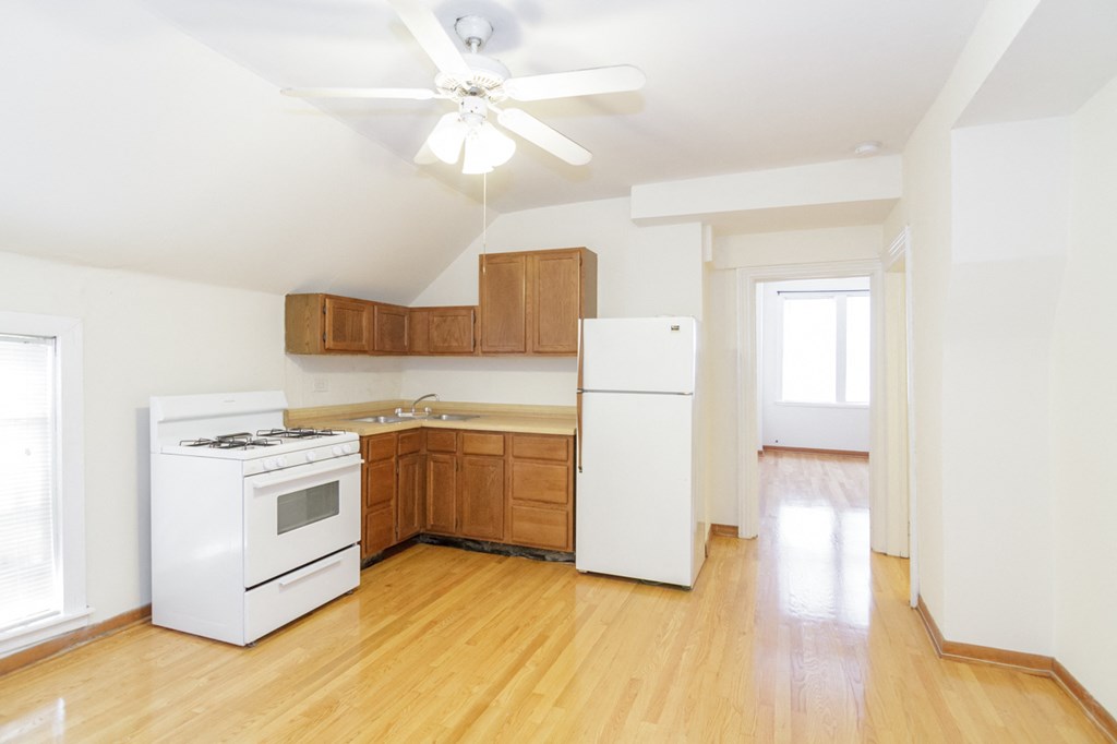 an empty kitchen with white appliances and wood floors
