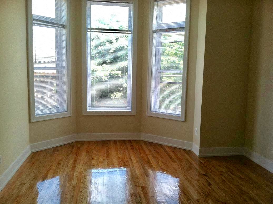a living room with three windows and a wooden floor