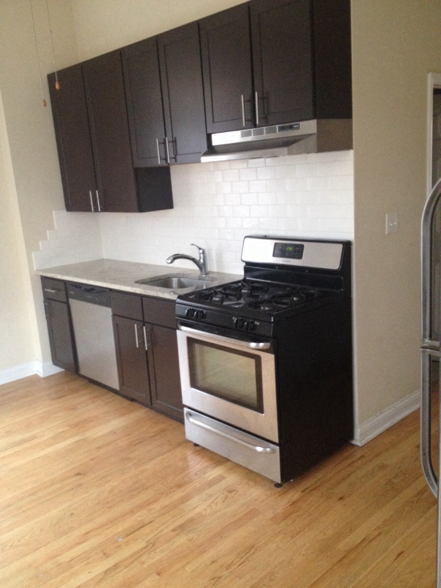 an empty kitchen with black and stainless steel appliances and wooden floors