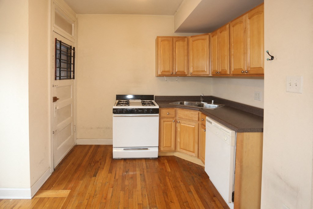 an empty kitchen with wooden floors and a white stove and sink