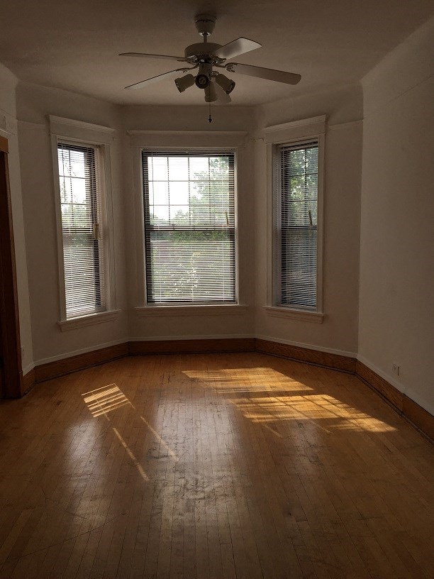 an empty living room with a ceiling fan and three windows