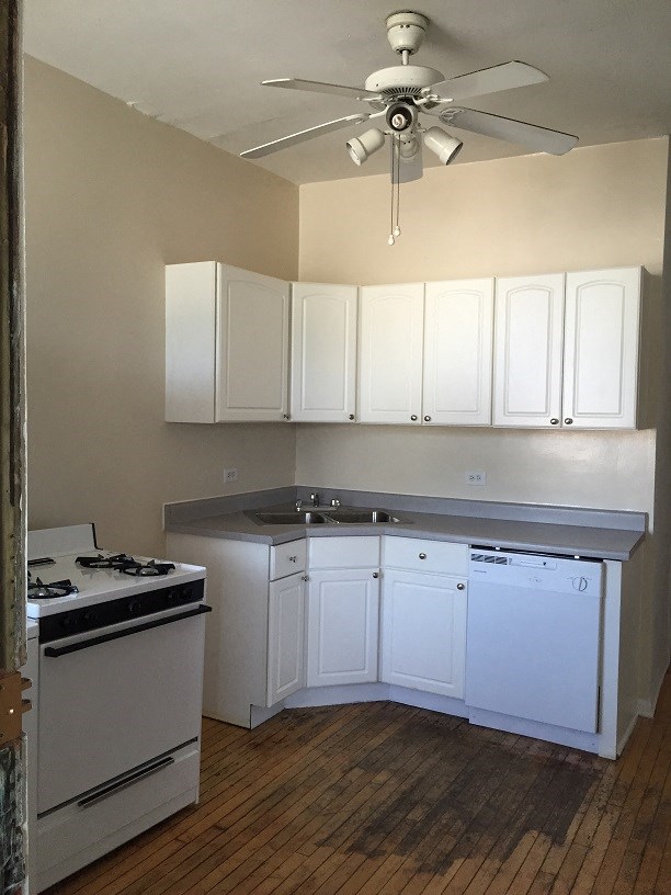 an empty kitchen with white cabinets and a ceiling fan