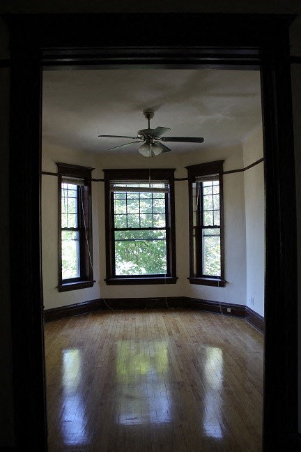 an empty living room with a ceiling fan and three windows