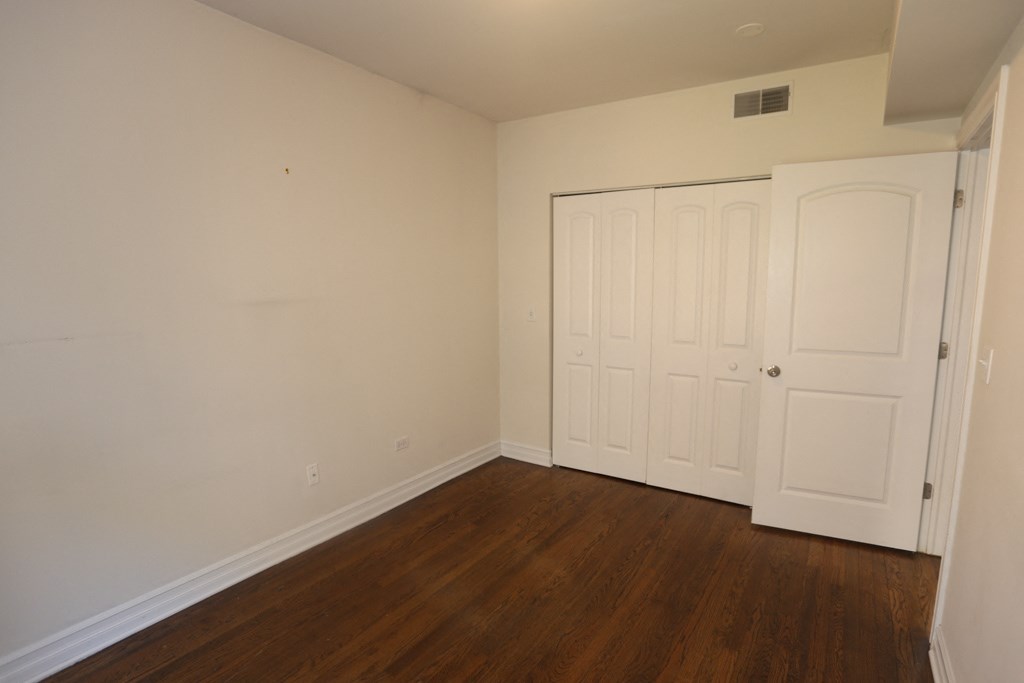 a bedroom with white walls and wooden floors and two closets