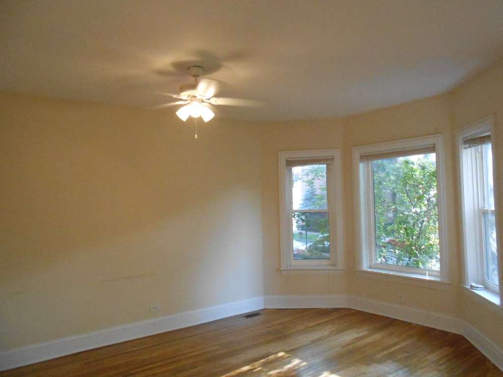 an empty living room with a ceiling fan and three windows