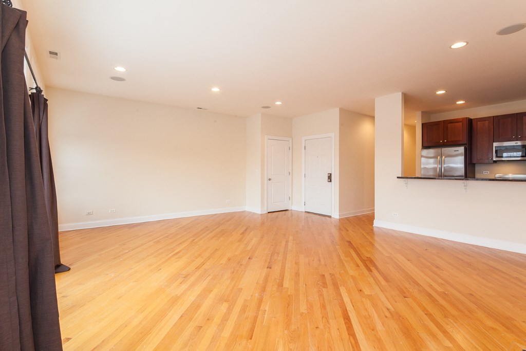 an empty living room with wood floors and a kitchen