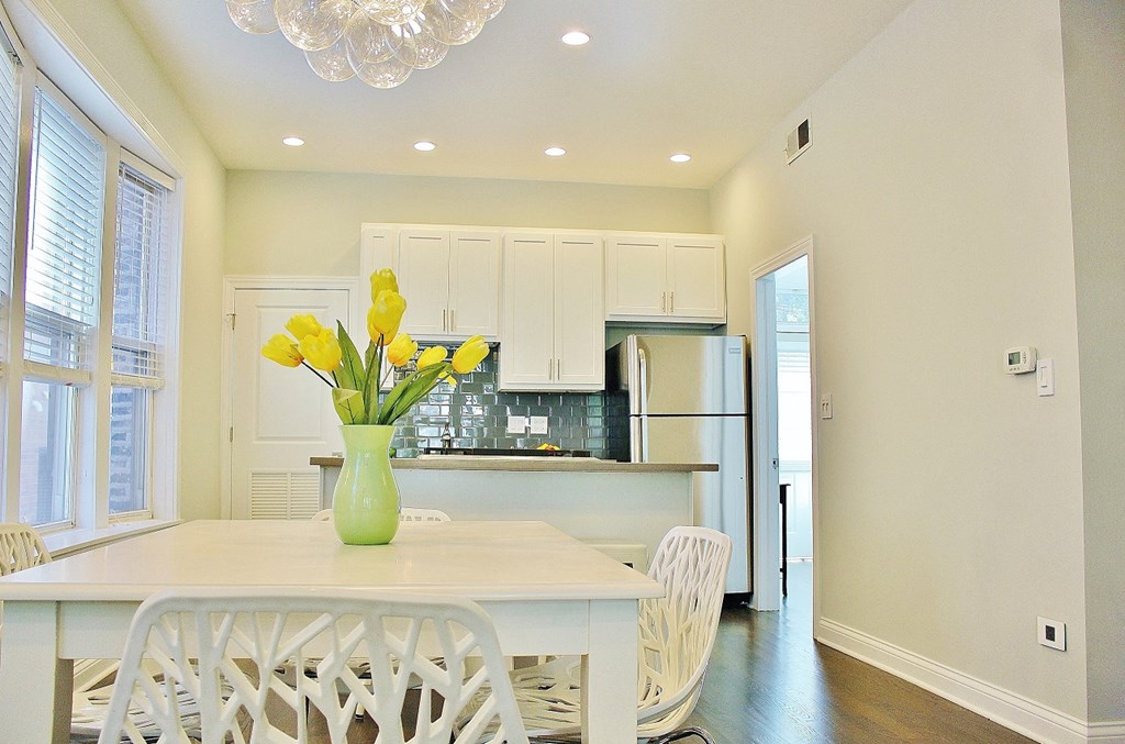 a kitchen with a white table and chairs and a vase with yellow flowers