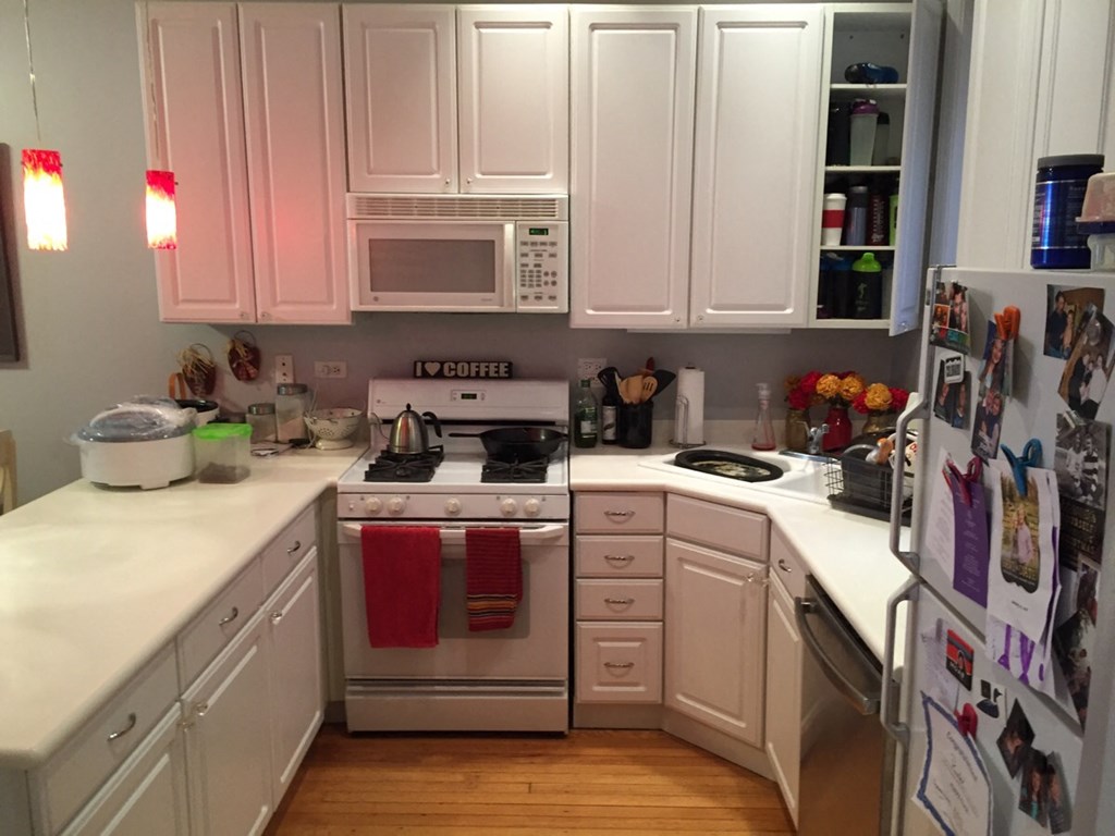 a small kitchen with white cabinets and appliances and a refrigerator