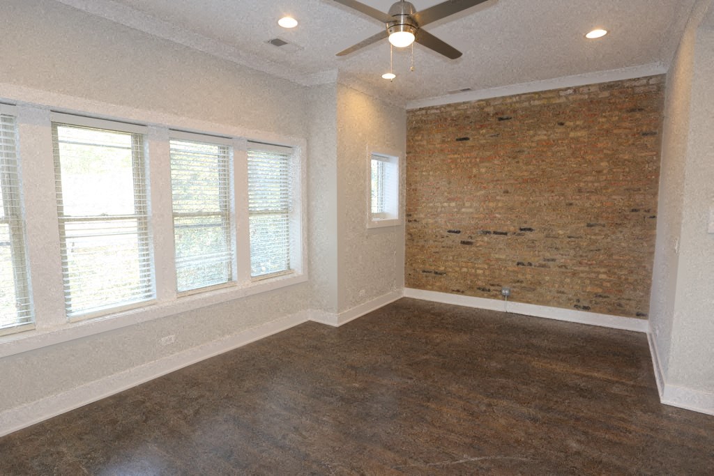 an empty living room with a brick wall and a ceiling fan