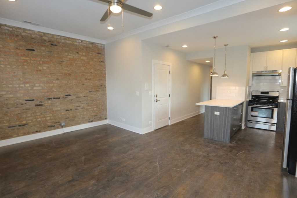an empty living room with a kitchen and a ceiling fan