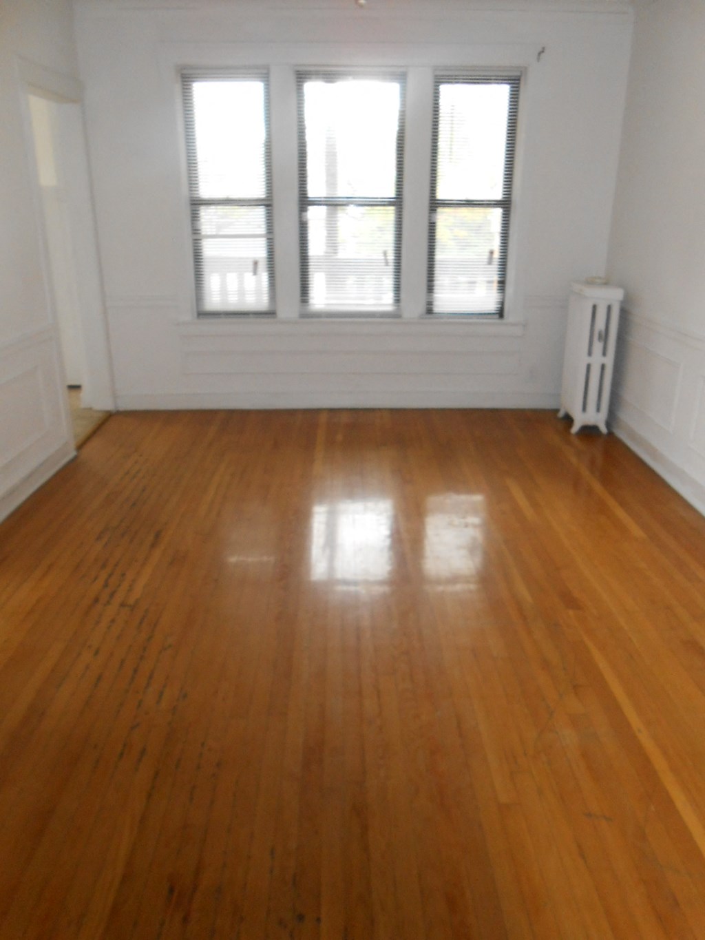an empty living room with wooden floors and three windows