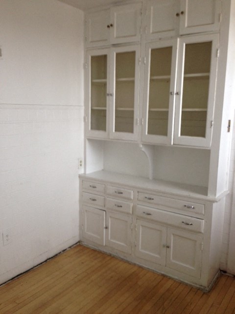 an empty kitchen with white cabinets and wooden floors
