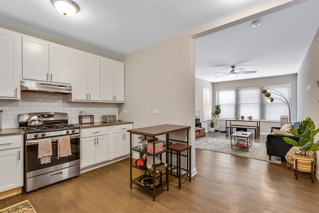 a kitchen with white cabinets and stainless steel appliances and a living room with a table