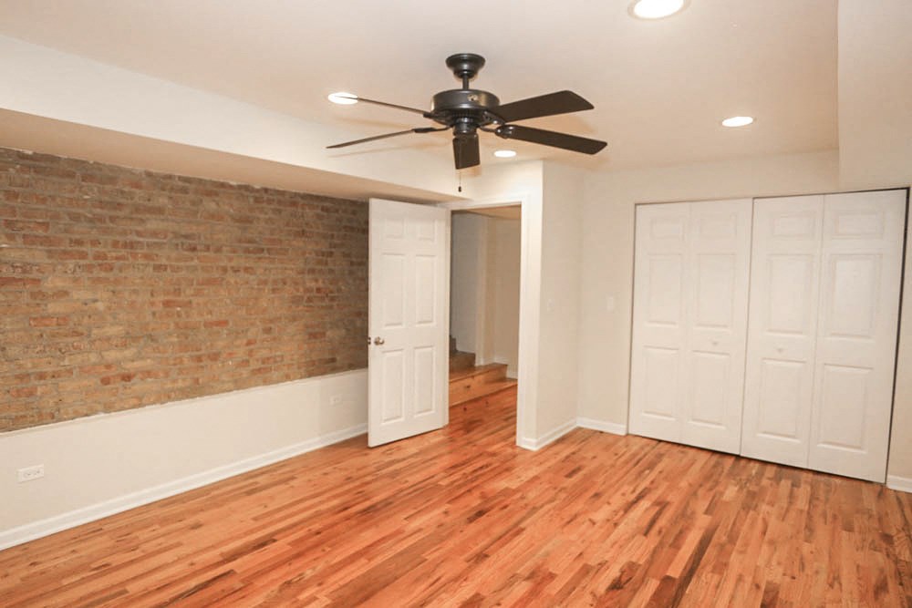 an empty living room with a ceiling fan and a brick wall