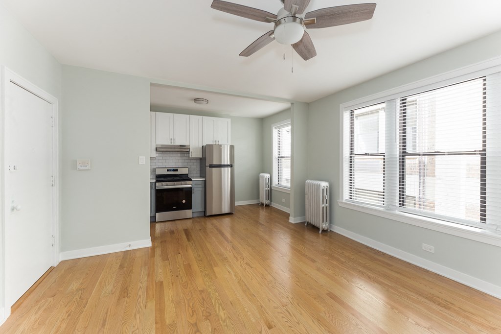 an empty living room with a ceiling fan and a kitchen