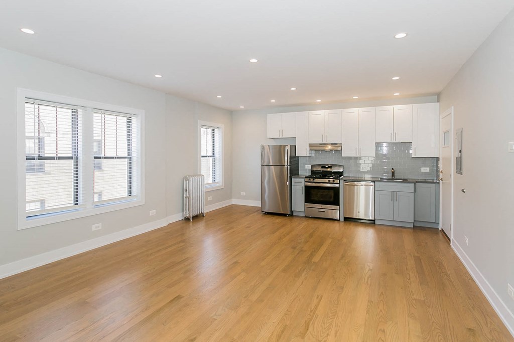 a living room with a hardwood floor and a kitchen with stainless steel appliances