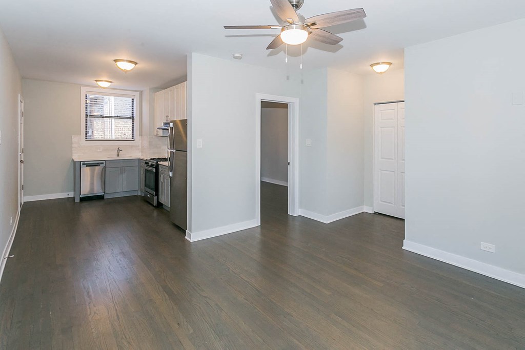 an empty living room and kitchen with wood flooring and a ceiling fan