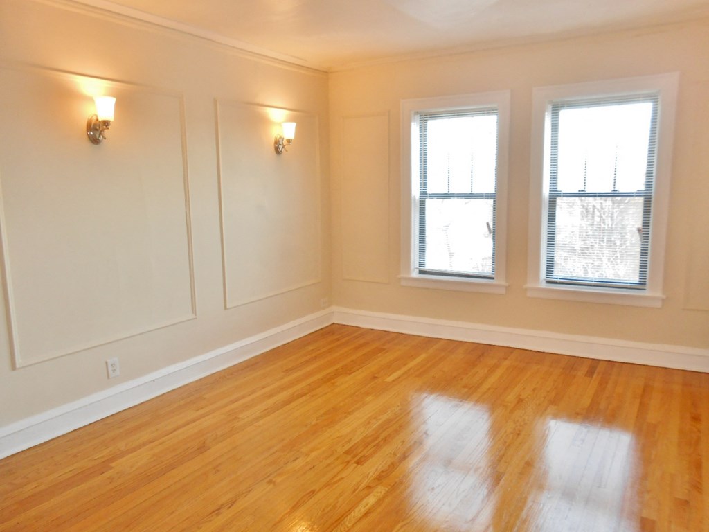 the living room of a house with a wooden floor and three windows