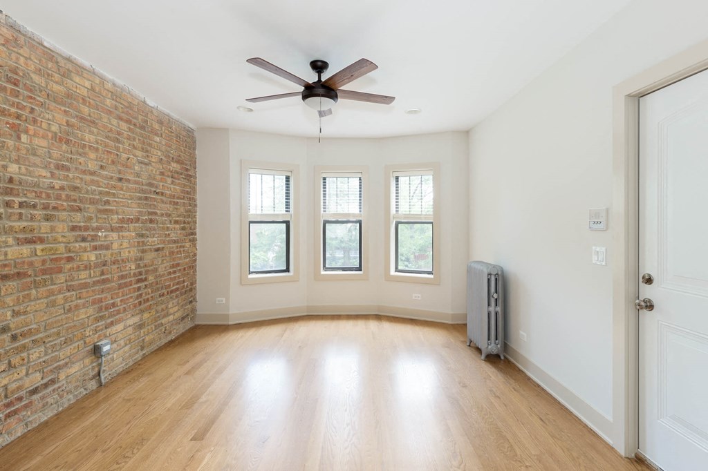 an empty living room with a ceiling fan and a brick wall